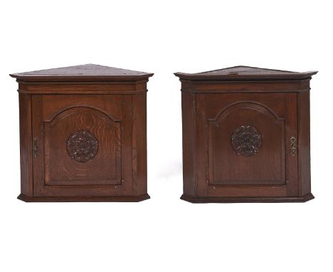 A pair of oak hanging corner cupboards, 20th c, the interior with serpentine shelf enclosed by a raised and fielded breakarch