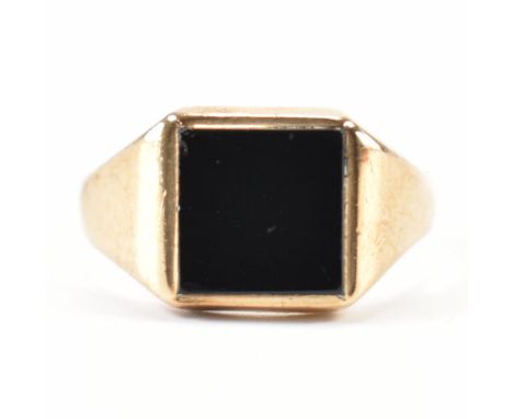 A hallmarked 9ct yellow gold &amp; onyx signet ring. The ring having a square bezel set black onyx panel to graduating should