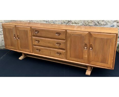An Ercol Windsor light elm, wide sideboard, having an arrangement of three drawers to centre, with a pair of cupboard doors t