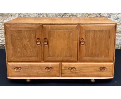 An Ercol Windsor light elm sideboard, having an arrangement of three cupboards, above a pair of short drawers, 76cm high x 13