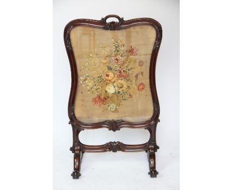 A Victorian carved mahogany fire screen, with scroll frame enclosing a tapestry and applique panel of flowers, on scroll feet