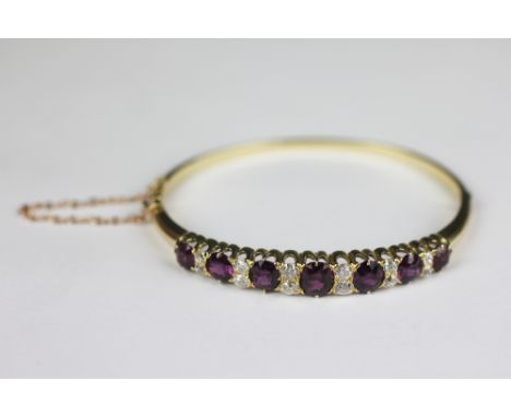 A pink sapphire or ruby and diamond set hinged bangle, the seven graduated, oval rubies each interspersed with two old cut di
