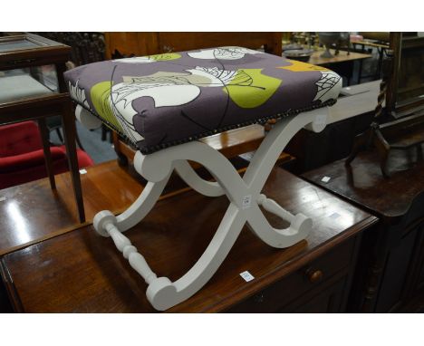 A painted X frame stool with abstract upholstery.