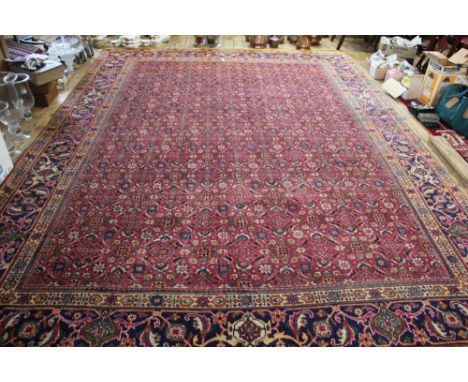 A Persian Tabriz wool carpet worked with a traditional foliate design against a red ground, 390cm x 282cm