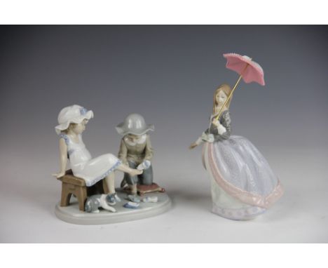 Two Lladro figures, to include; a boy and girl trying on shoes 5361 14.5cm high and a girl with a parasol 5211, 22.5cm high (