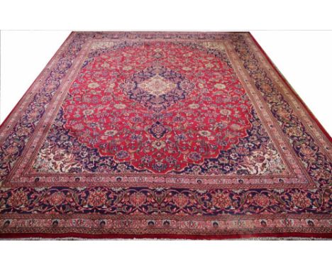 A large Kashan hand woven wool carpet, with a central medallion and all over foliate design against a red ground, 395cm x 285