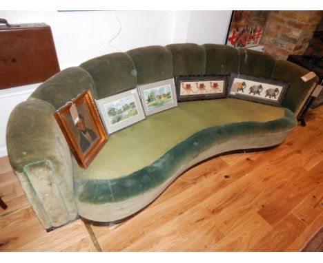 An Art Deco curved upholstered sofa, covered in green fabric  and raised on an eboised plinth, L. 250cm