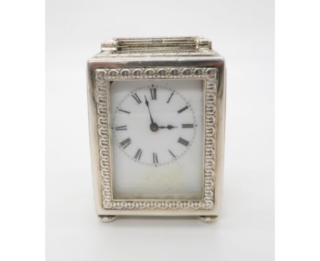 AN EDWARDIAN SILVER MINUET CARRIAGE CLOCK, the circular white enamelled dial with Roman numerals, the case and handle lined w