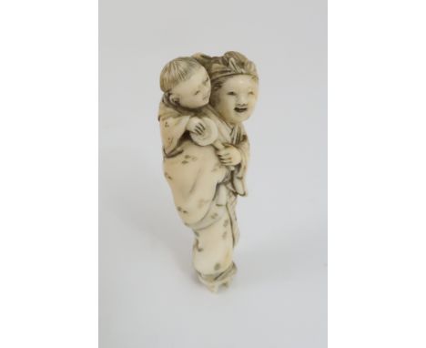 A JAPANESE IVORY NETSUKE carved with a mother carrying a child on her back, signed, on a red lacquered tablet, 5cm high Condi