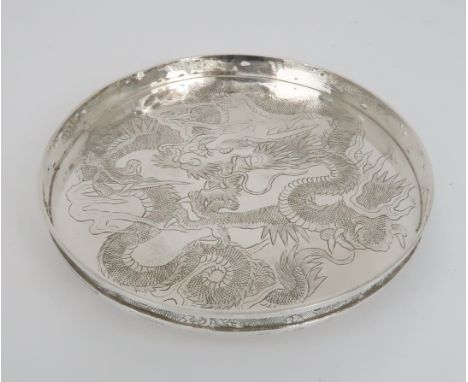 A CHINESE SILVER CIRCULAR TRAY decorated with a dragon chasing the flaming pearl, within a pierced border and on three ball f