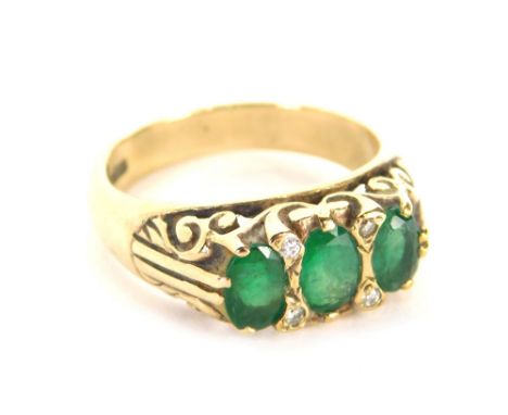 An emerald and diamond gypsy ring, set with four round brilliant cut tiny diamonds, and three oval emeralds, with scroll desi