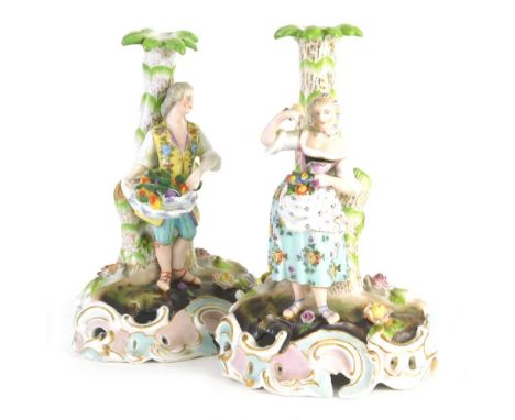 A pair of Meissen style porcelain candlestick groups, formed as a lady and gentlemen, each dressed in finery, on naturalistic