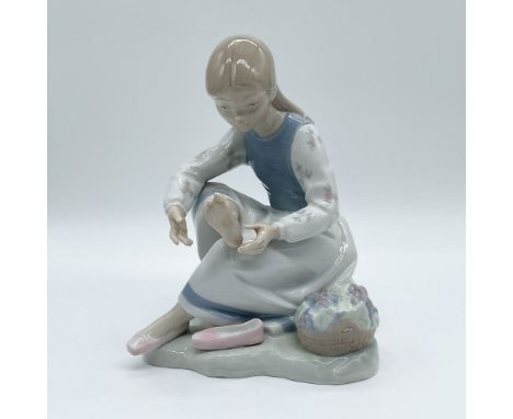 Delightful Japanese porcelain figurine depicting a young girl tending to her foot while seated next to a basket of colorful f