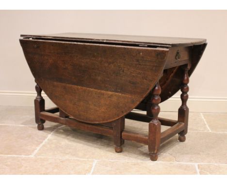 An 18th century oak drop leaf dining table, the oval plank top above a single frieze drawer, upon bobbin and baluster turned 