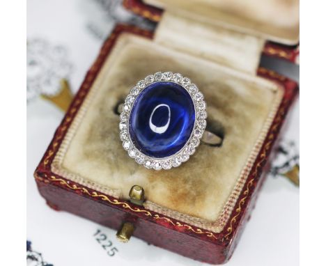 An early 20th century sapphire and diamond cluster ring, the central oval sapphire cabochon measuring 13.8mm x 11.7mm x 7.9mm