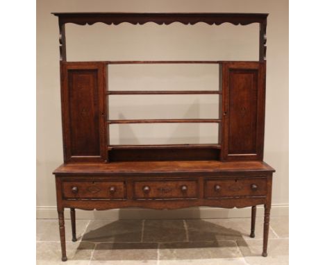 A George III oak and mahogany crossbanded dresser, the open plate rack with a moulded cornice and wavy frieze above four shel