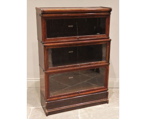 A Globe Wernicke walnut three tier stacking bookcase, early 20th century, each tier with an 'up and over' glazed door, upon a