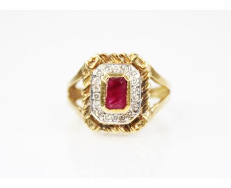 A ruby and diamond cluster ring, the central emerald cut ruby measuring 6mm x 3.5mm, set to a surround of eighteen brilliant 