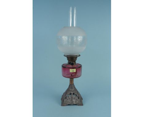 A 19th Century oil lamp with a cranberry red reservoir above a cast iron base and etched globe