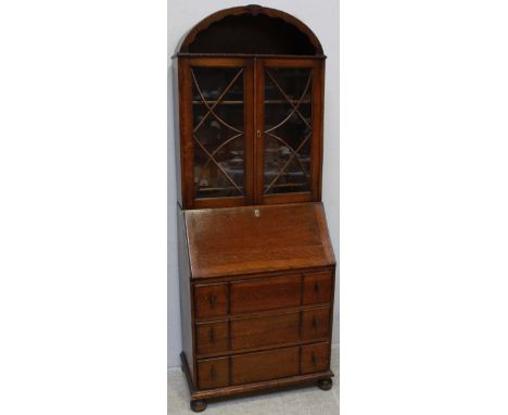 A 1920s oak veneered bureau bookcase, with arched top and open shelf, fall-front enclosing pigeonholes, above three long draw