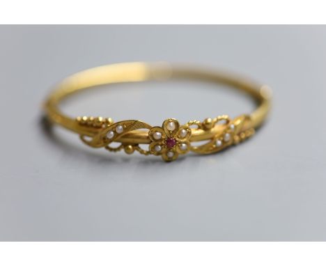 A late Victorian yellow metal, ruby and seed pearl set hinged bangle, gross 10.6 grams.CONDITION: There are 3 splits and a de
