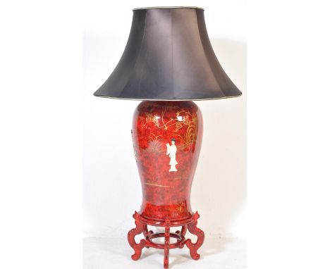 A 20th century red lacquered floor standing cinnabar vase lamp with oversized shade, the base raised on a wooden socle plinth