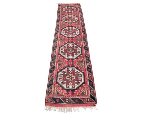 A TURKISH RUNNER OF USHAK STYLE woven in gold, blue, brown and off white with five guls and filler motifs on a madder ground 