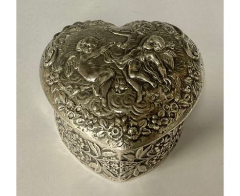 An Edwardian silver love heart shaped trinket box and cover, repousse worked with three cherubs amongst foliate scrolls, gild