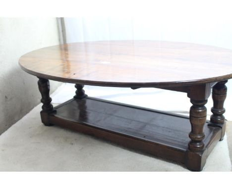 An oval dropleaf solid wood low/coffee table with turned uprights and solid lower tier shelf, length 116cm, ht 43cm 