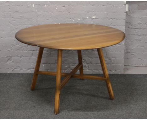 An Ercol Golden Dawn drop leaf circular dining table, raised on reeded square supports.