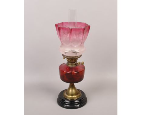 A Victorian cranberry glass oil lamp raised on black glass and brass trumpet shaped base.Condition report intended as a guide