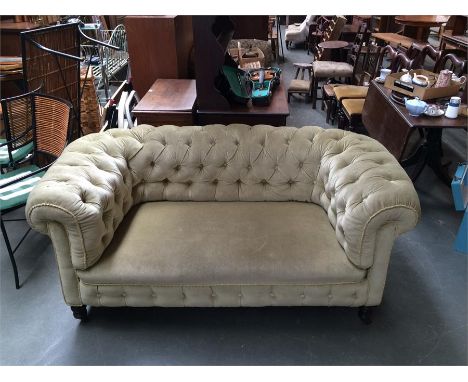 A two seater chesterfield with button back, raised on turned legs at the front, upholstered in green fabric