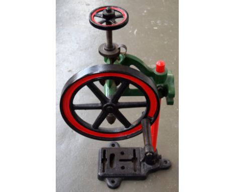 A vintage hand cranked bench drill press, painted in black, red, and green