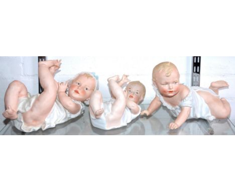 Three Gebruder Heubach bisque piano babies, c1910, with blue intaglio eyes and painted and moulded hair and shift, two on the