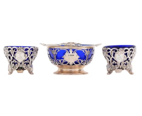 A pair of Victorian cast silver openwork salt cellars, on three feet, blue glass liners, crested, 83mm diam, by James Charles