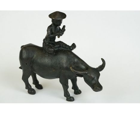 An ornamental Chinese cast metal sculpture of a man playing a flute riding an ox. 