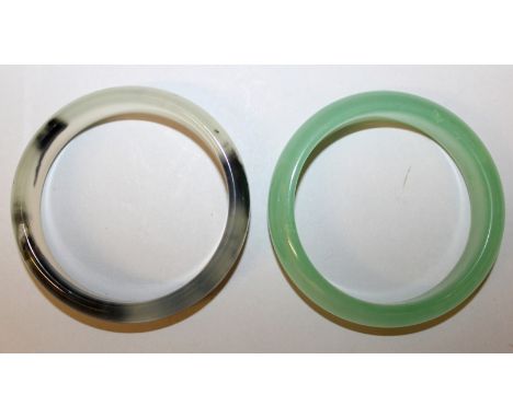 TWO CHINESE JADE-LIKE BANGLES, one apple green the other grey with black inclusions, each 3.1in diameter, each inner rim 2.4i
