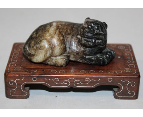 A 19TH/20TH CENTURY CHINESE JADE MODEL OF A BUDDHISTIC LION, together with a wire inlaid rectangular wood stand, the creature