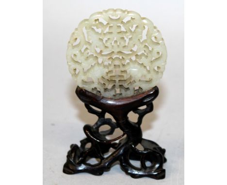 A 19TH/20TH CENTURY CHINESE PIERCED CELADON JADE CIRCULAR PLAQUE, together with a fixed wood stand, the plaque carved with au