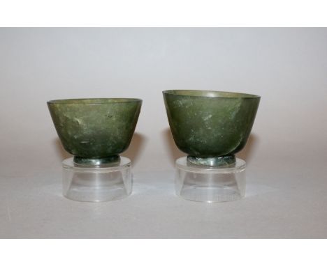 A PAIR OF EARLY 20TH CENTURY CHINESE GREEN JADEITE CUPS, on fixed perspex stands, the predominantly green and semi-transparen