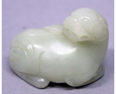 A CHINESE CELADON JADE-LIKE MODEL OF A MYTHICAL CREATURE, it's head turned backwards over it's body to fend off a giant moth,