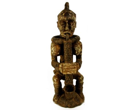 An Igbo female Ikenga figure, Nigeria, modelled smoking a large pipe seated on a stool with traces of paint, height 72cm, wid