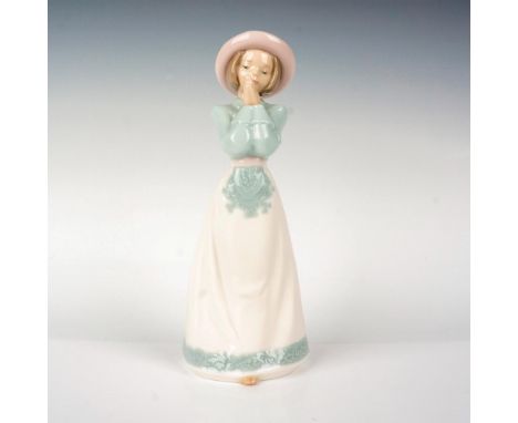 A figurine of a young woman in a blue dress, white apron, and pink hat with her hands together by her face. Nao by Lladro bac