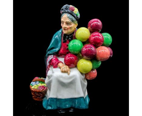 Glazed, hand painted figurine. The elderly woman is in a green shawl over her burgundy blouse and matching white and green sk