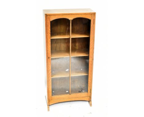 A 1920s light oak narrow bookcase, with glazed door on standard end supports, height 114cm, width 53cm, depth 23cm.Additional