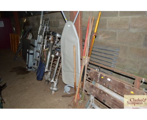 A bundle of long handled gardening tools and a ironing board