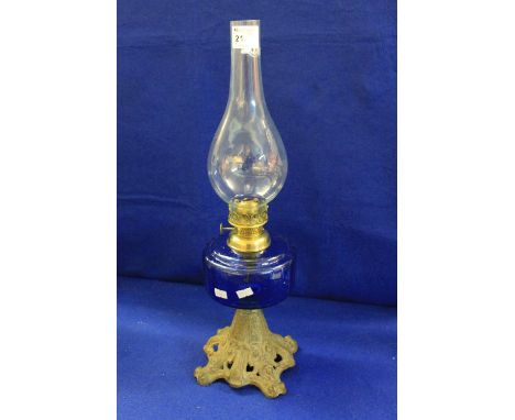 Brass single burner oil lamp with blue glass reservoir, cast metal base and clear glass chimney. 