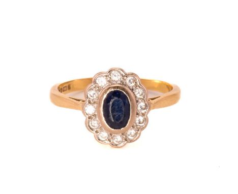 A sapphire and diamond cluster ring in 18ct gold, featuring an oval sapphire in a dark blue colour, collet set within a circl