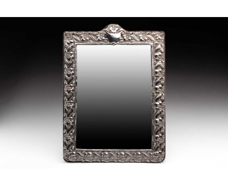 A silver-framed dressing table mirror of rectangular form, the arched crest with vacant cartouche and repousse repeating flow