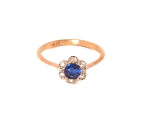 A sapphire and diamond flower head ring, featuring a round sapphire claw set in the centre and surrounded by six old-cut diam